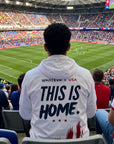Person wearing a white jacket with 'This is Home' text at a sports event in a stadium.