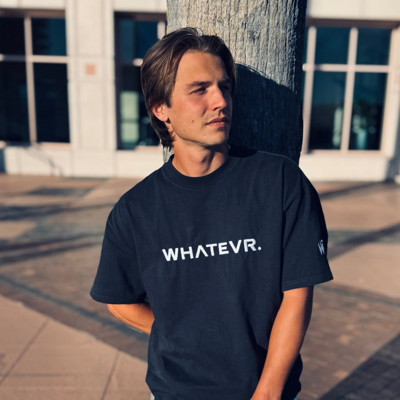 Man wearing a black t-shirt with 'WHATEVR.' text standing outdoors.