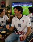 People watching a sports game on TV in a living room, wearing jerseys with USA designs.